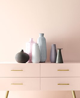 A light pink wall frames a pink console with gold handles and multiple vases.