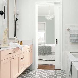 A white-painted bathroom with pale pink cabinets opens to a gray bedroom with contemporary chandelier. A white-painted bathroom with pale pink cabinets opens to a gray bedroom with contemporary chandelier.