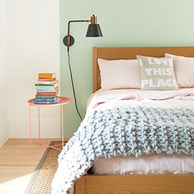 A bed set against a light green feature wall. A bed set against a light green feature wall.