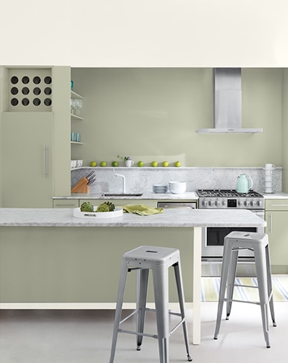 A sage green-painted kitchen with bar seating, silver appliances, and a variety of kitchen utensils.