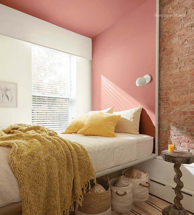 Chambre à coucher avec mur en briques, table d'appui en bois, lit blanc, oreillers et couverture jaunes et paniers entreposés sous le lit.
