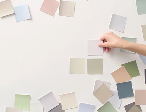 A person applying various color swatches on a white wall.