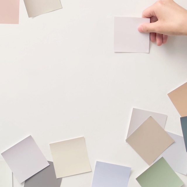A person applying various color swatches on a white wall.
