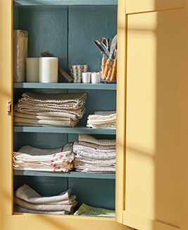 An open linen cabinet painted in Chestertown Buff HC-9 and Aegean Teal 2136-40.