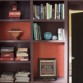 A brown bookshelf with two red accent squares; books and baubles line the shelves. A brown bookshelf with two red accent squares; books and baubles line the shelves.