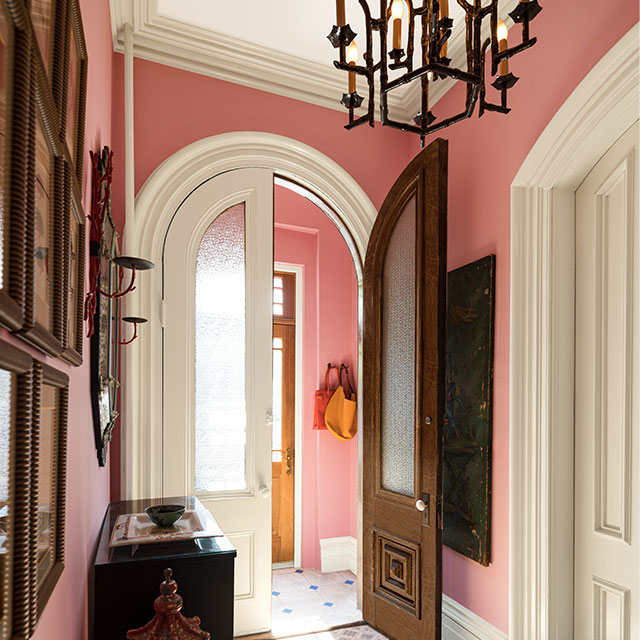 An entryway painted in Delicate Rose, with Niveous trim, a collection of wall art, large doors, and ornate chandelier.
