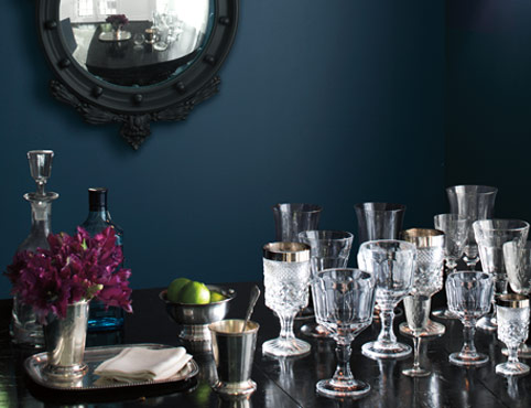 Une pièce peinte en bleu foncé arborant un miroir encadré noir et des verres en cristal posés sur une table.