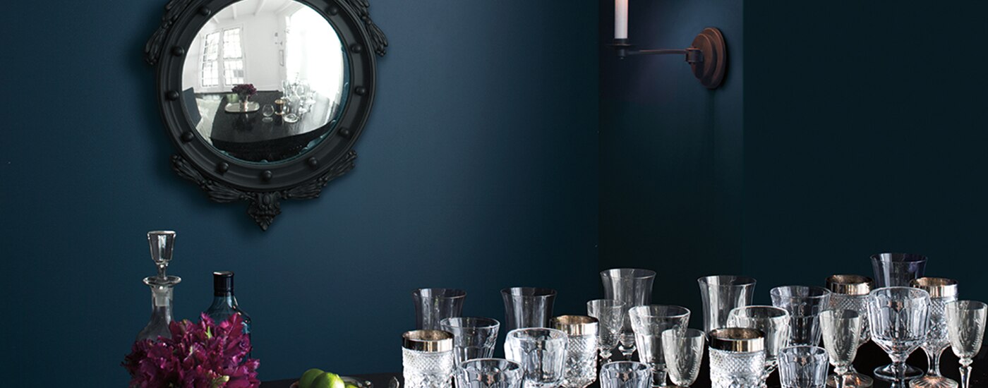 Une pièce peinte en bleu foncé arborant un miroir encadré noir et des verres en cristal posés sur une table.