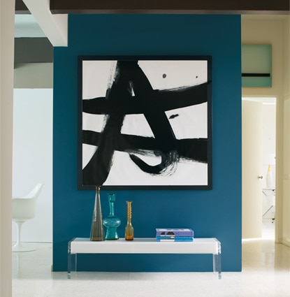 A bold blue accent wall offsets a black and white graphic painting in a bright hallway. A bold blue accent wall offsets a black and white graphic painting in a bright hallway.