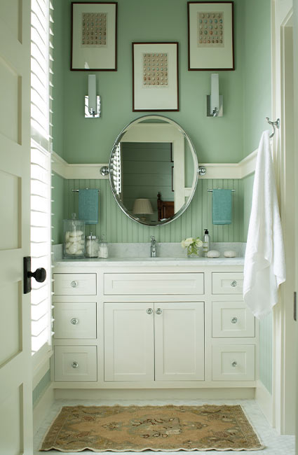 Ванная комната цвета морской пены с круглым зеркалом и тремя рамами для фотографий, висящими над белым туалетным столиком.