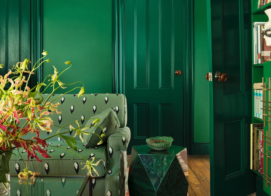 A green-painted living room with green-printed couch, stone end table, glass coffee table, and bookshelves matching the walls. 