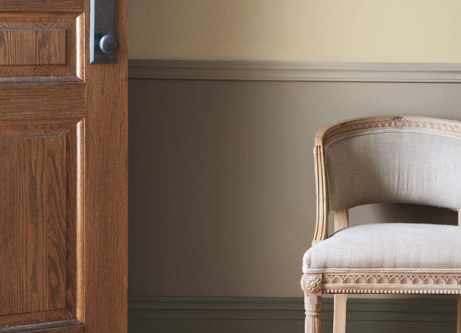 Un hall d’entrée taupe présentant une porte en bois, des lambris et une chaise beige.