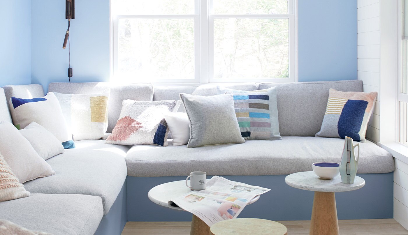 A living room with two blue walls and one white shiplap wall, featuring a large, gray sectional couch and three small end tables.