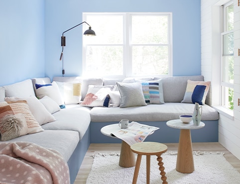A living room with two blue walls and one white shiplap wall, featuring a large, gray sectional couch and three small end tables.