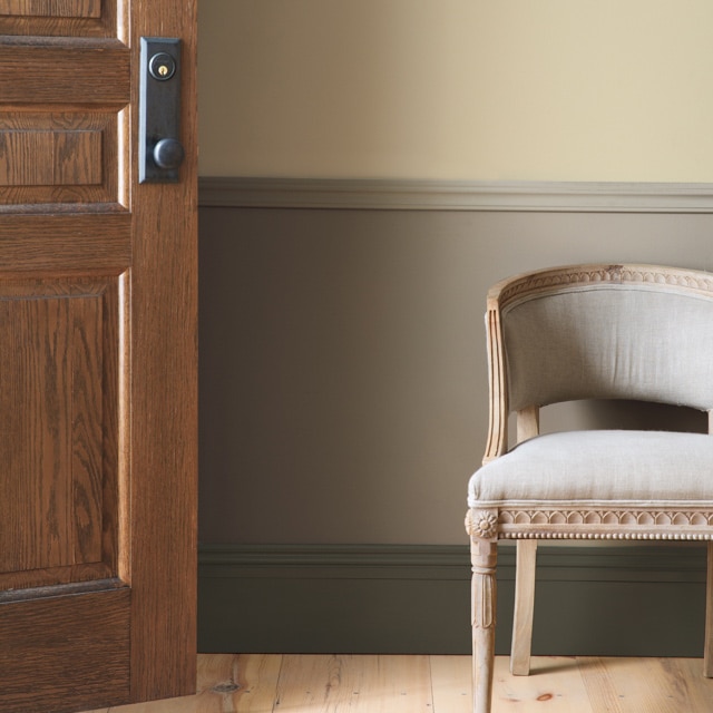 Un hall d’entrée taupe présentant une porte en bois, des lambris et une chaise beige.