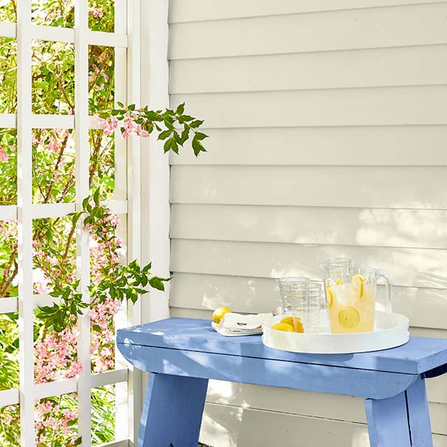 Un parement extérieur blanc cassé et un banc bleu sur lequel repose une carafe de limonade.