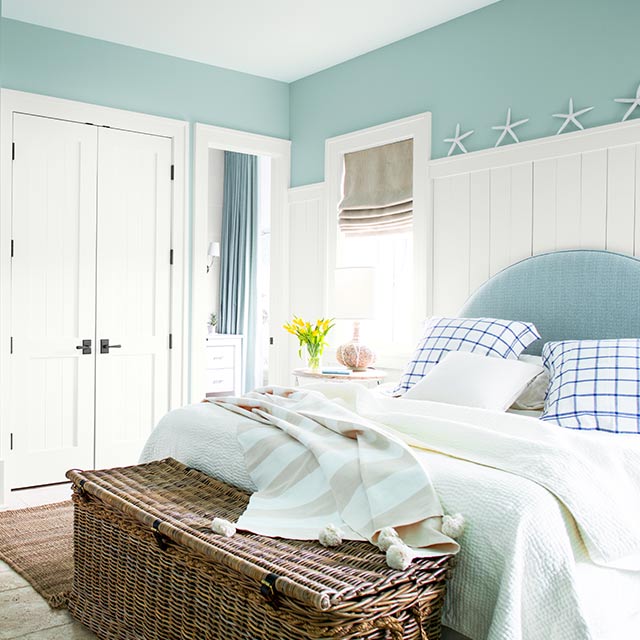 Une chambre aux murs peints en bleu clair arborant un bureau blanc encastré et un grand lit sur lequel reposent un édredon et des coussins bleu pâle et foncé.