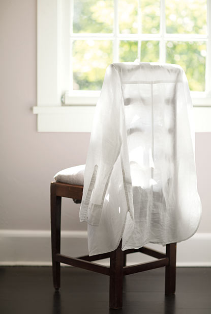 Dark wood chair with white linen draped over the back in a light gray room with white window.