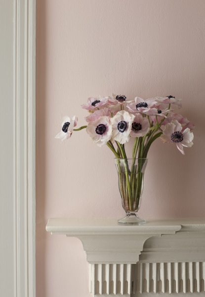 Murs roses en sourdine avec un manteau de cheminée blanc contenant un vase de fleurs roses assorties.