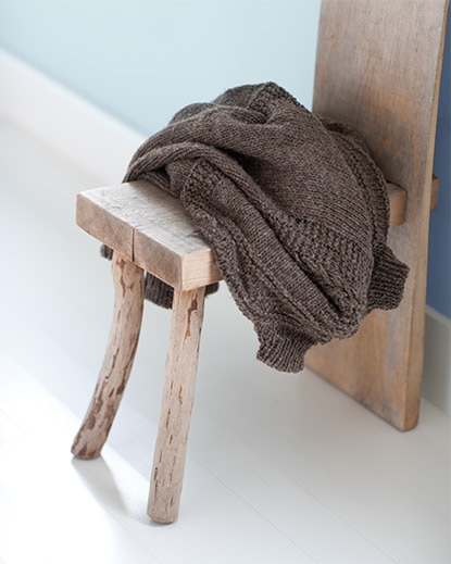 A rustic wood chair with a brown sweater casually tossed across its seat stands out against a white floor and light blue wall. A rustic wood chair with a brown sweater casually tossed across its seat stands out against a white floor and light blue wall.
