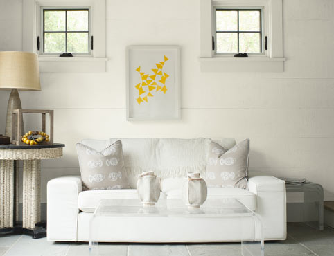 A bright sitting room with white shiplap walls accented by neutral fabric furniture and accessories.