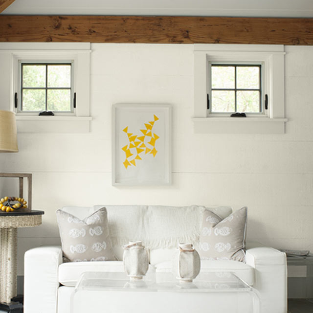 A bright sitting room with white shiplap walls accented by neutral fabric furniture and accessories.