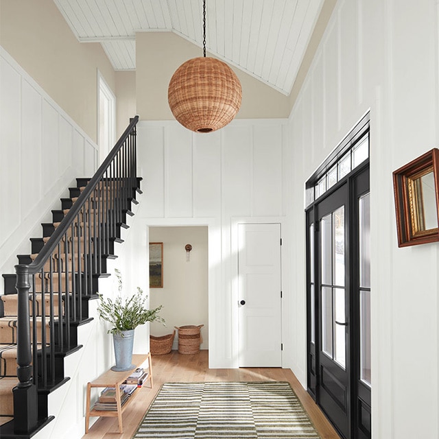 A home entryway with off-white painted upper walls, white board-and-batten lower walls, a white shiplap ceiling, a black stairway, and a black front door.