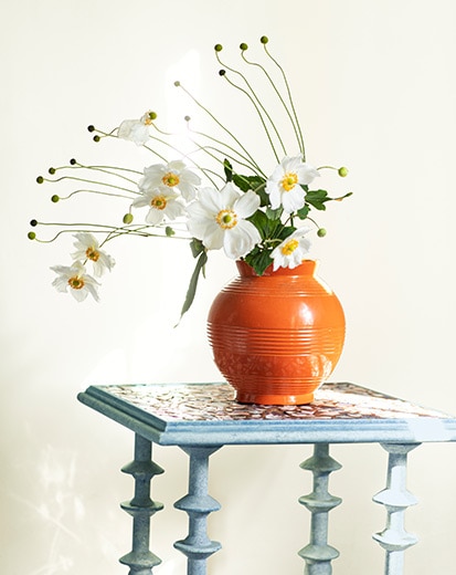 A blue table with a vase full of white flowers against an off-white-painted wall.