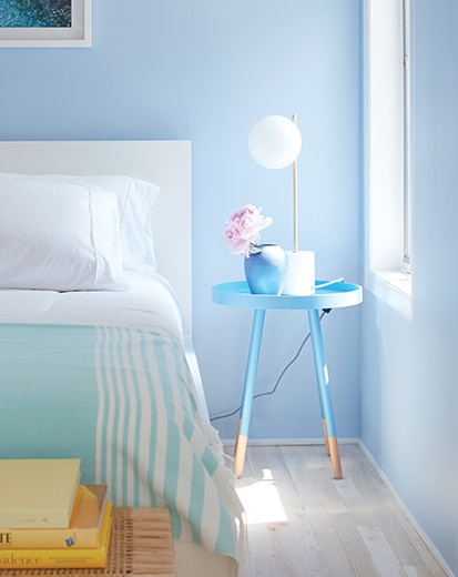 A blue-painted bedroom with blue and white bedding, light wood floors, and a blue night table.