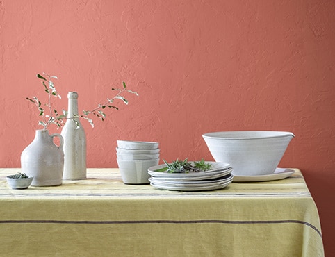 Des vases décoratifs et des bols de service blancs sur une table devant un mur peint d’un rouge doux.