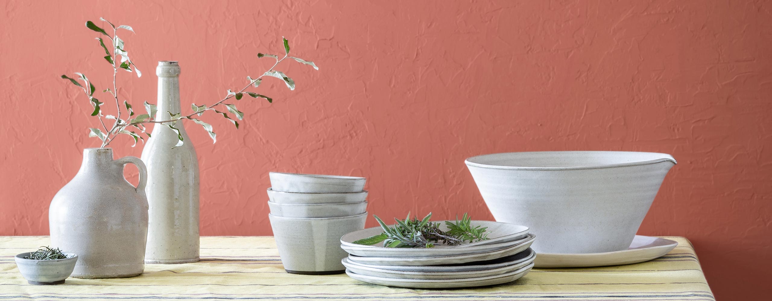 Des vases décoratifs et des bols de service blancs sur une table devant un mur peint d’un rouge doux.