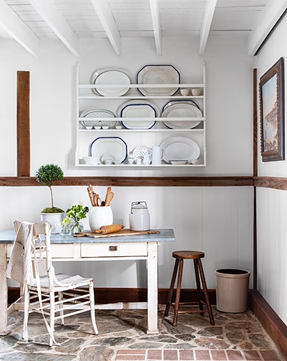 A white-painted room with built-in white shelving, wood trim, stone floors, and a white desk and chair.