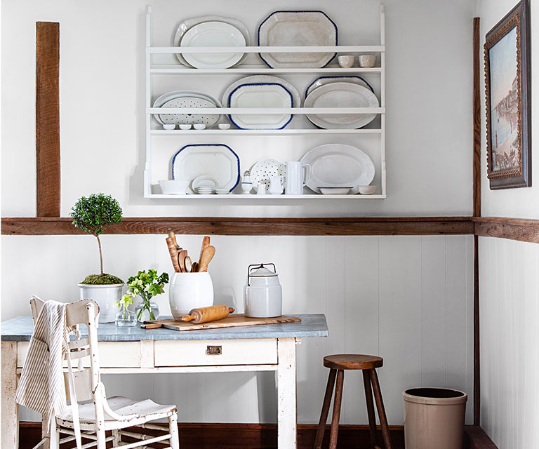 A white-painted room with built-in white shelving, wood trim, stone floors, and a white desk and chair.