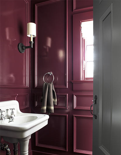 A bold plum-painted panelled bathroom featuring a white antique sink.