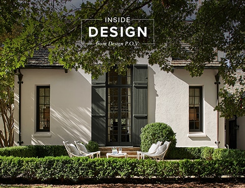 A sun-dappled home exterior painted in a creamy beige with deep sage green-painted doors and trim with an alfresco seating area.