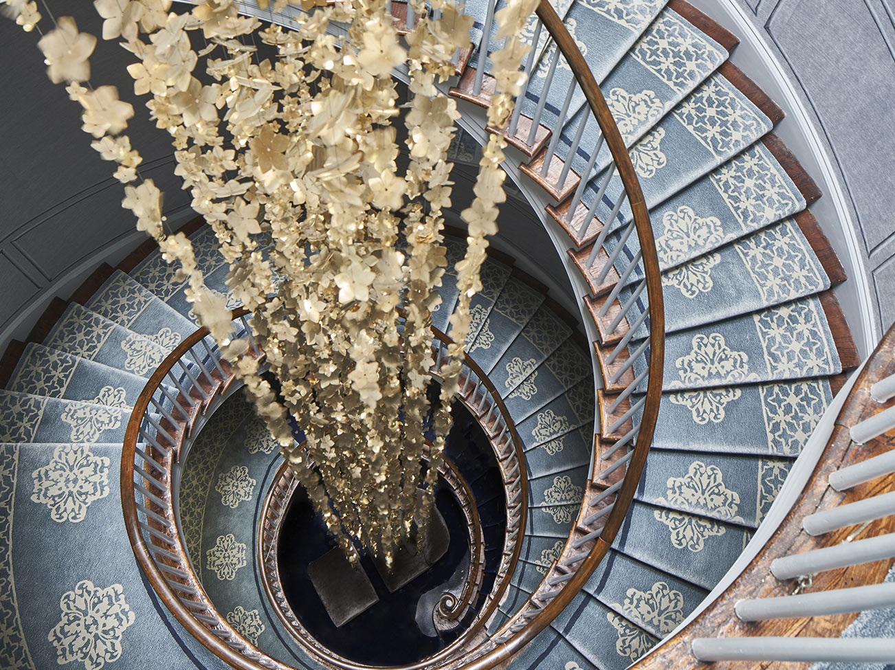 A 40' brass Cherry Blossom mobile, with 4,000+ metal flowers, cascades down the centre of a spiral staircase at the 2019 Kips Bay Decorators Show House NYC. 