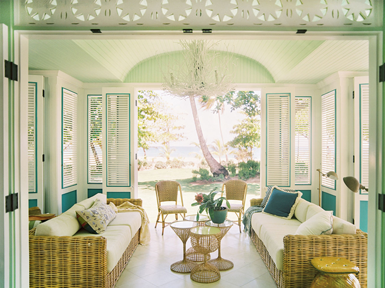An island veranda in green and creamy white hues with hinged shutter panels, two woven wicker sofas and matching chairs. An island veranda in green and creamy white hues with hinged shutter panels, two woven wicker sofas and matching chairs.