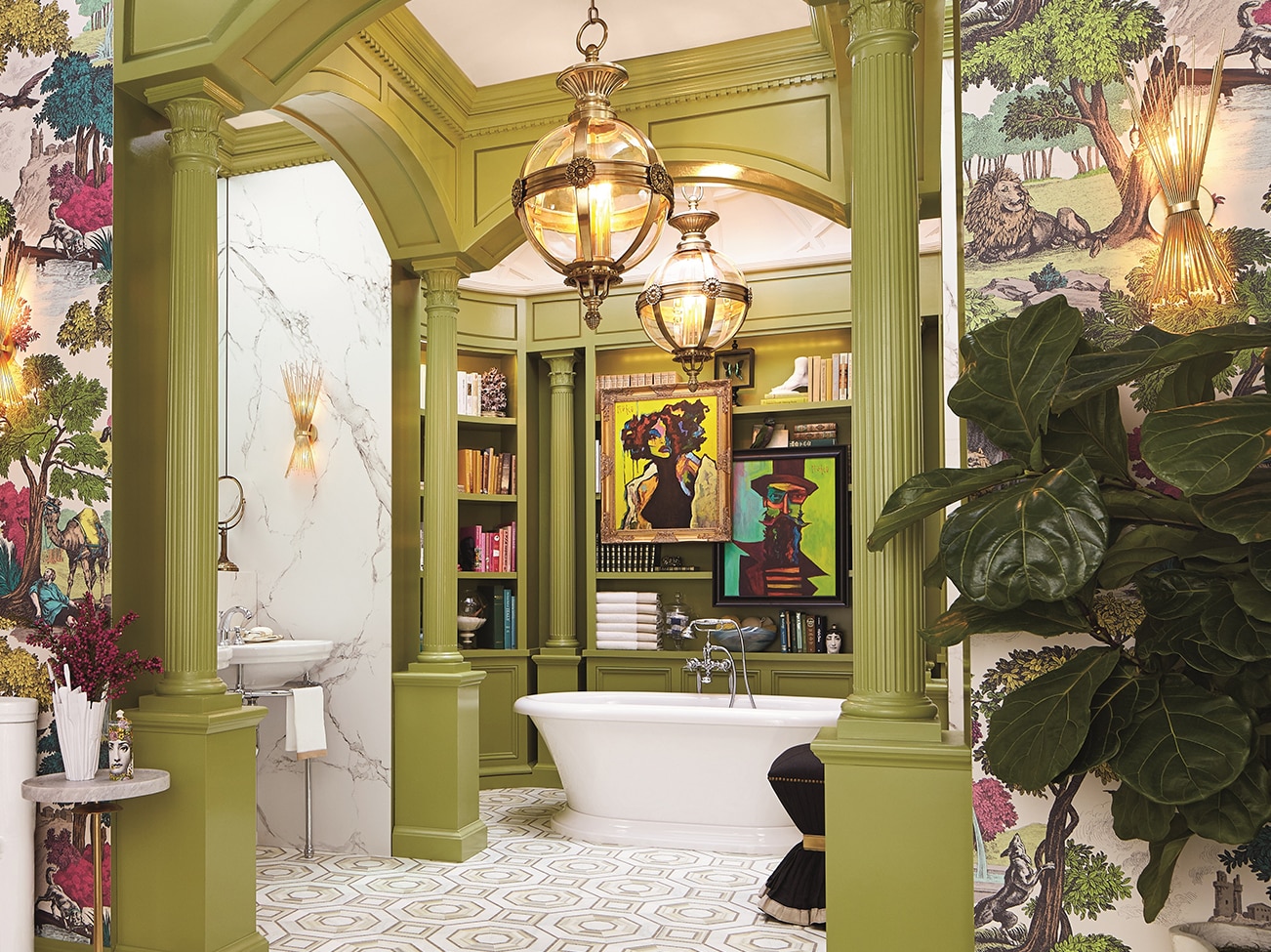 Salle de bains principale aux colonnes et alcôves peintes en vert, baignoire ovale blanche avec œuvres d’art et étagères, papier peint aux motifs végétaux et plancher aux carreaux géométriques.