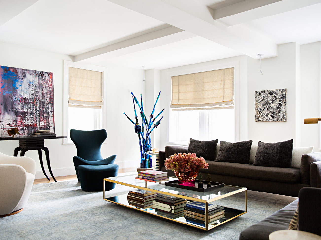 White-painted living room with coffered ceiling, brown sofa, modern chairs, gold-framed glass coffee table & abstract art.