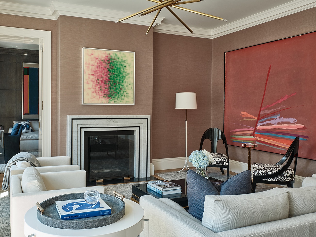 An earthy, taupe-painted living room with off-white couches, two black reading chairs with print cushions, and a fireplace.