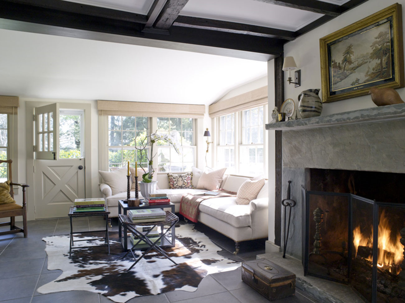 Sitting room with white-painted walls and ceiling, stone fireplace, animal print rug, Dutch door, and light-filled windows.