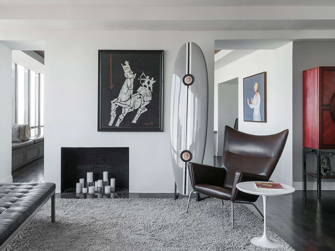 A light-filled sitting area with off-white walls, gray leather tufted bench, fireplace, and modern leather chair.