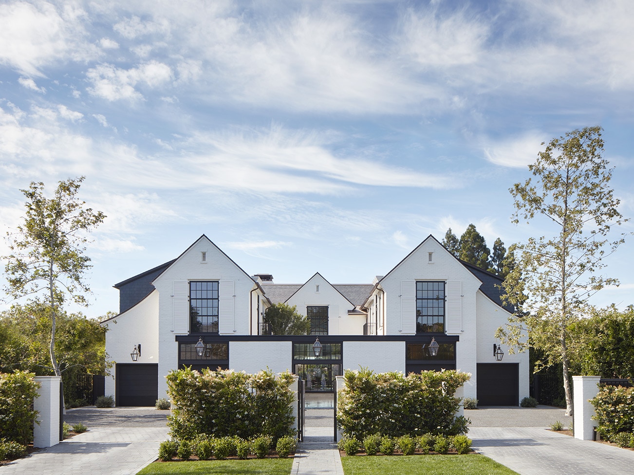  Exterior view of a white-painted multi-wing house with black trim, gabled roofline, and balanced landscaping.