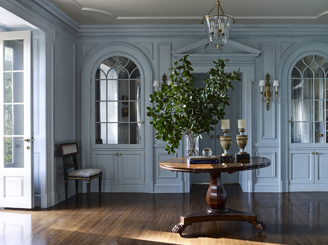 Entryway with painted moulding surrounding matching Palladian style mirrored windows, flanking pediment topped doorway and circular entry table.