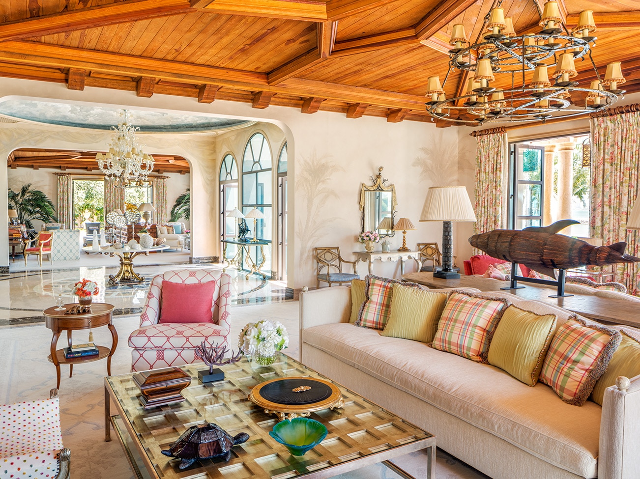 Neutral living room with raspberry accents, oversized sofa, wood coffered ceiling, and French doors with patterned draperies.