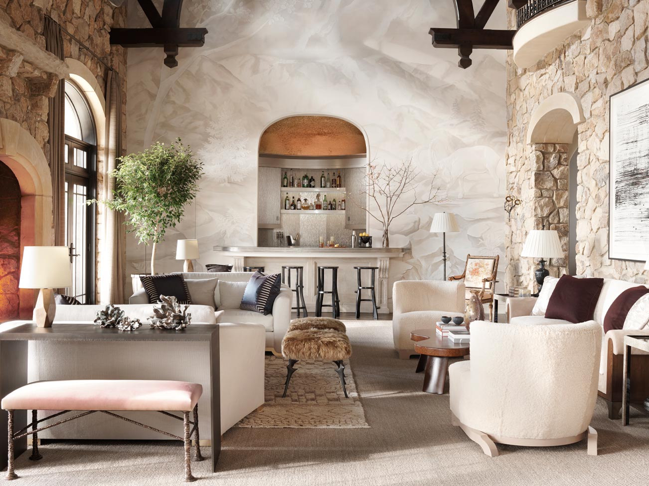 Grand salon d’inspiration espagnole avec murs et foyer en pierre, mur d’accent recouvert de stuc de finition, bar et sièges multiples de couleur blanche.