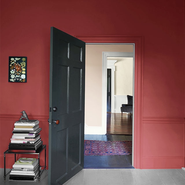 A pomegranate-coloured wall with an open dark gray-painted door and table with books.