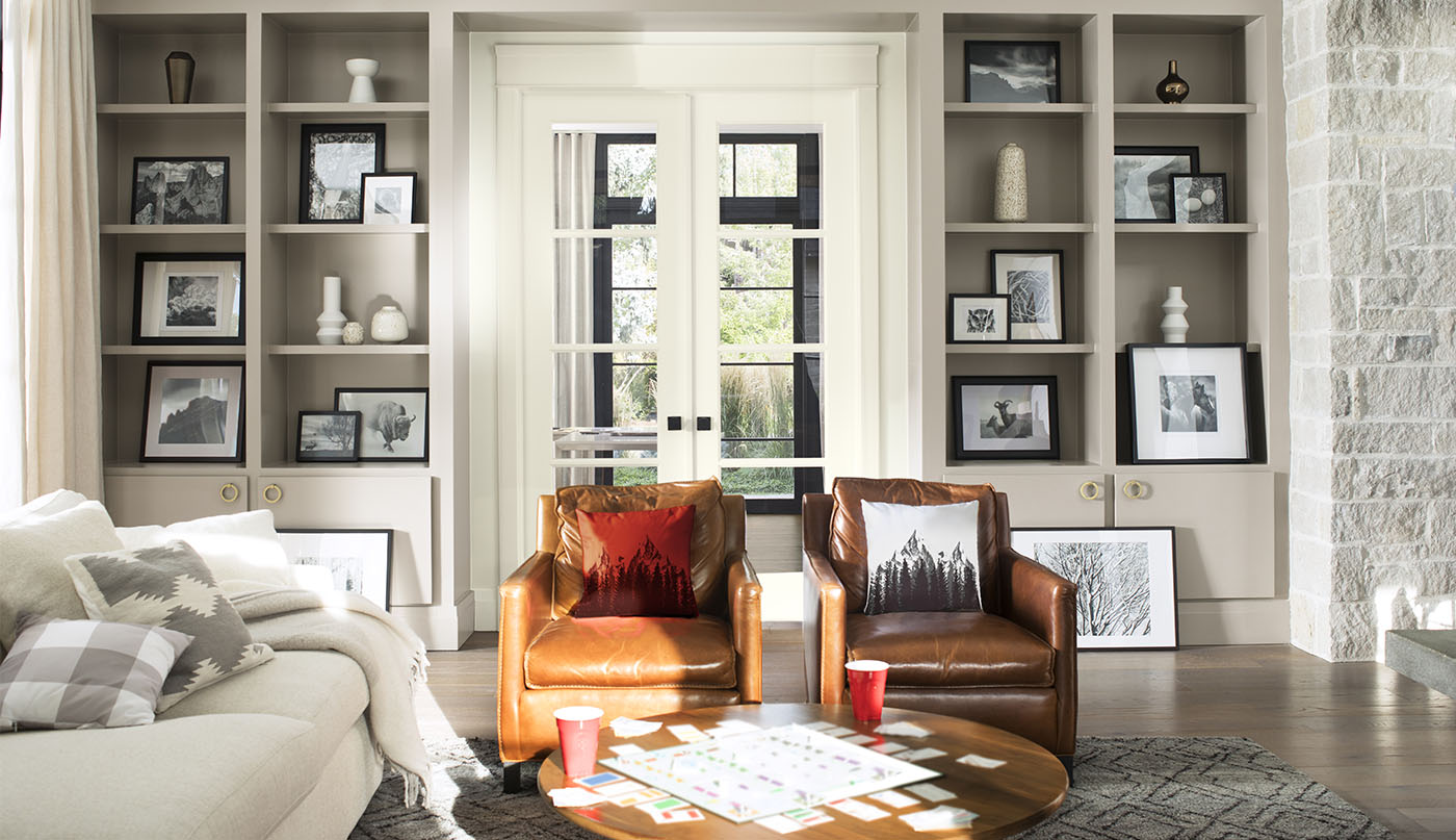 A comfy living room with gray-painted built-in bookshelves, white french doors, a white sofa, and brown leather chairs.