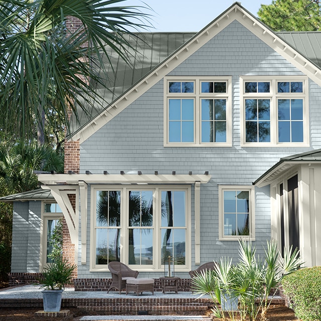 Pretty light-gray painted house with white trim, shaded by palm trees. 