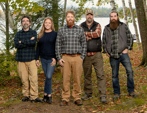 The 5-person cast of Maine Cabin Masters, who also own the Kennebec Cabin Company, pose in the woods.